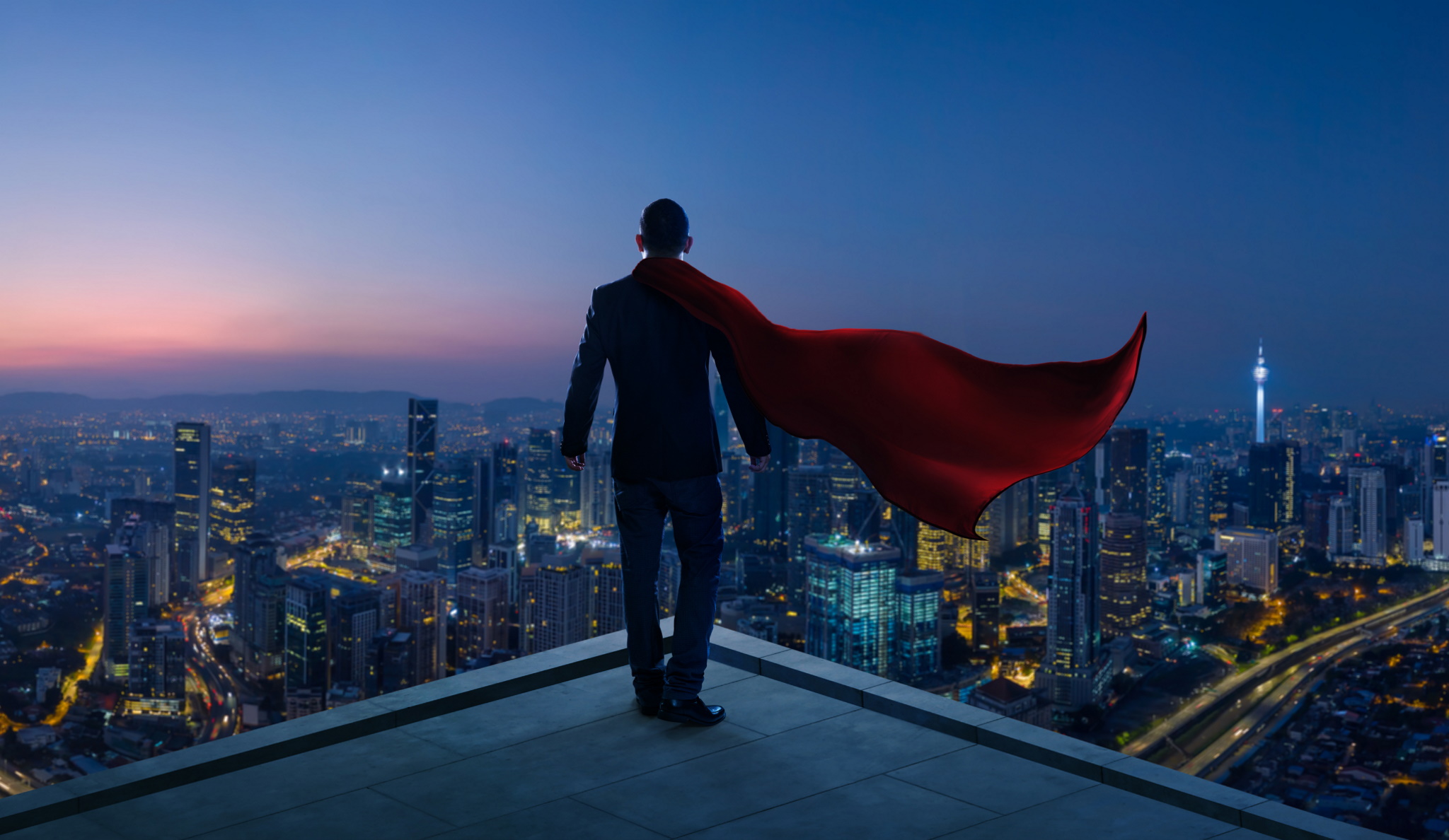 Businessman in suit and cape hero stand at rooftop looking great cityscape view and thinking business plan of the future . Night scene .